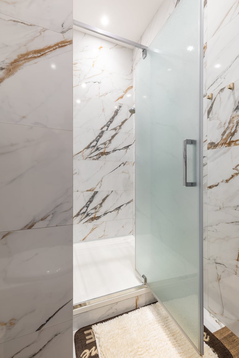 Luxurious shower area featuring marble walls and frosted glass door