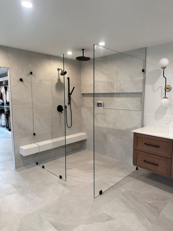 Modern bathroom with large walk-in shower featuring glass enclosure, rainfall showerhead, and wooden vanity with white countertop