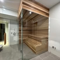 Modern glass-enclosed sauna with wooden interior benches in a contemporary bathroom