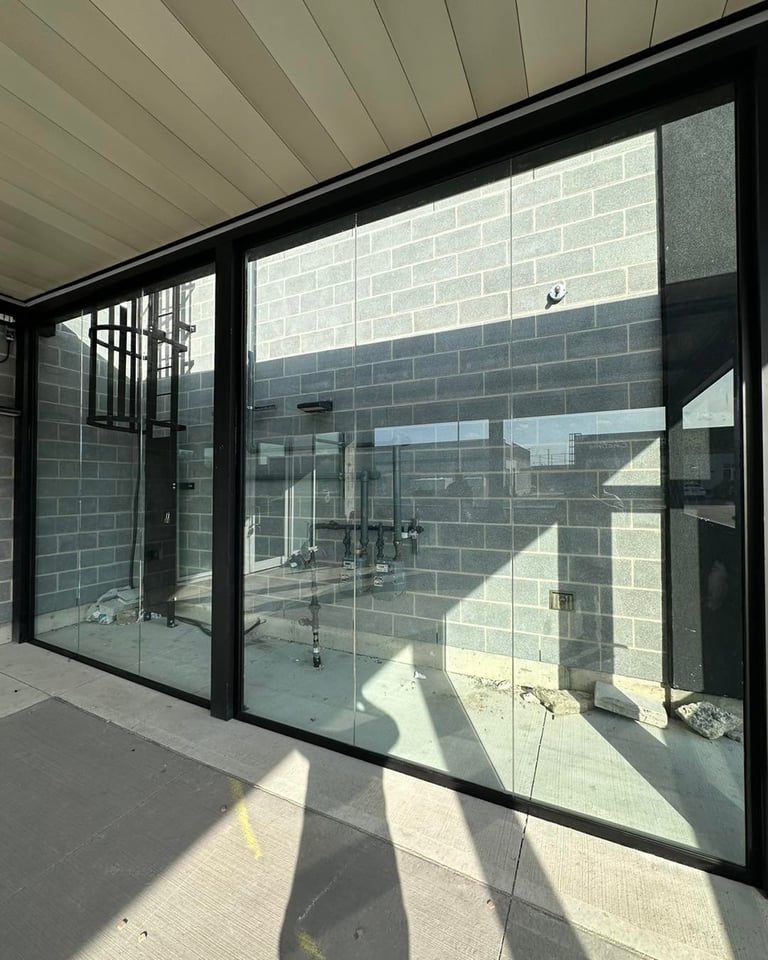 Large black-framed glass doors and windows on a covered patio overlooking a brick building courtyard with sunlight streaming across the pavement