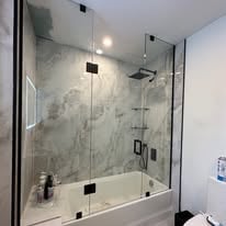 Modern glass-enclosed shower stall with marble tile walls, chrome fixtures, and black hardware details