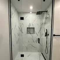 Modern bathroom shower with white and grey marble tile walls, glass enclosure, and black fixtures